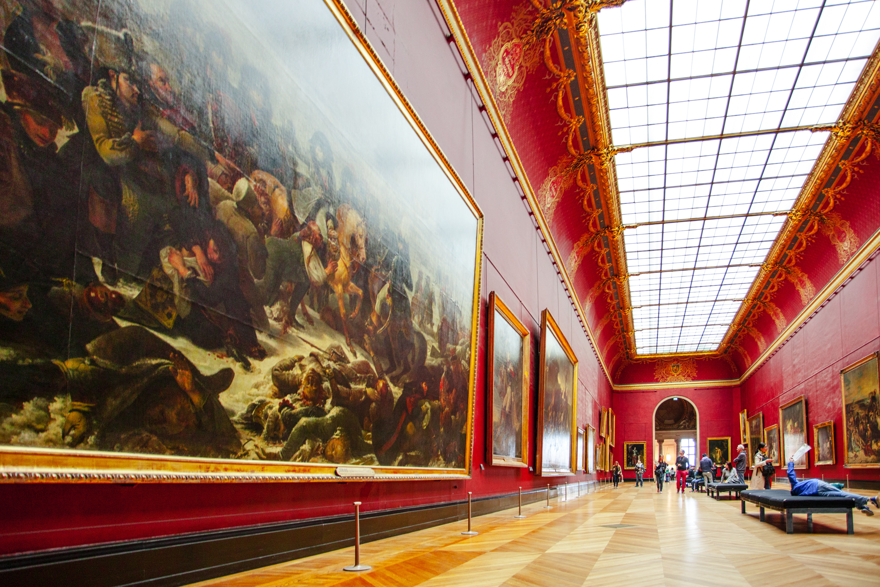 Visitors inside a red gallery space in the Louvre Museum. 